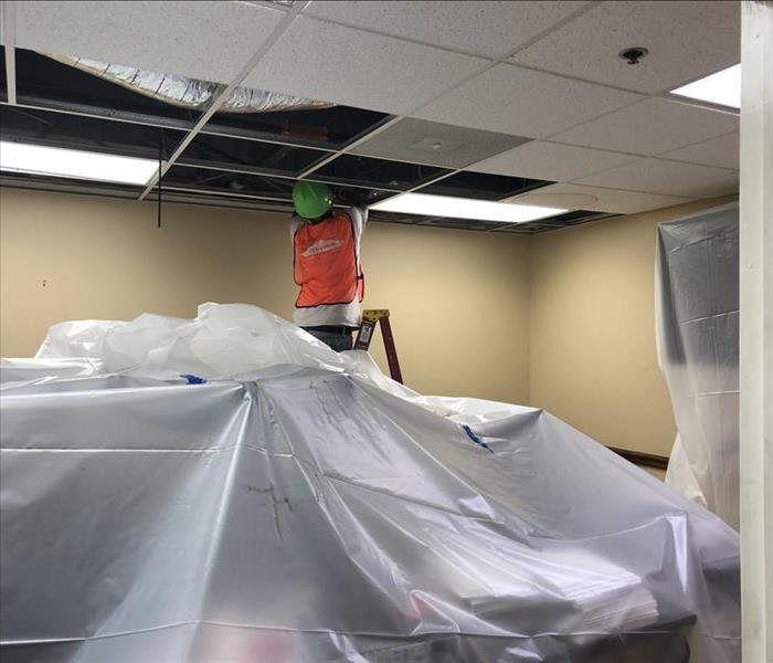 SERVPRO employee lifting ceiling tiles and setting up vapor barriers during water damage restoration project
